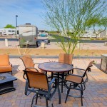 Beautiful outdoor patio with outdoor seating set with orange cushions. Table with four chairs around and matching sofa with a fire-pit in front. Large gas barbeque.