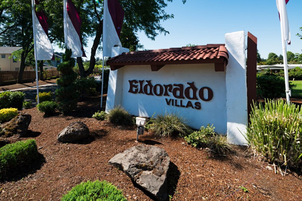 Eldorado Villas in Tigard, OR is a 55 plus manufactured home community with a sign at the entrance and purple and white flags.