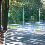 Windy roads in and out of Heritage Village. Tall trees along the roads. Tall green and blue flags are in the median. Lots of shade.
