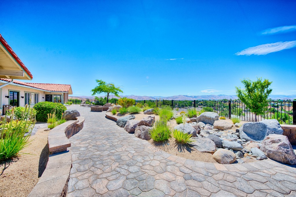 A cobblestone walkway takes you around the community center with desert landscaping on both side. Small shrubs and rocks. Views of the mountains.
