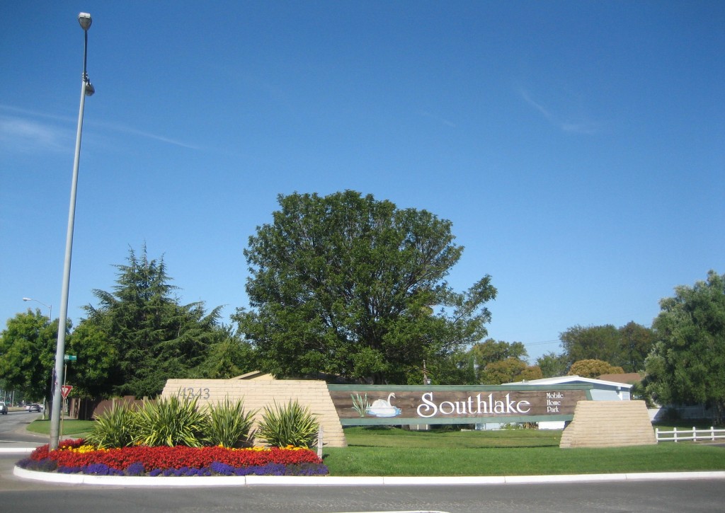 Large front entrance sign into Southlake Mobile. Surrounded by beautiful red, purple, and yellow flowers and well maintained grass.