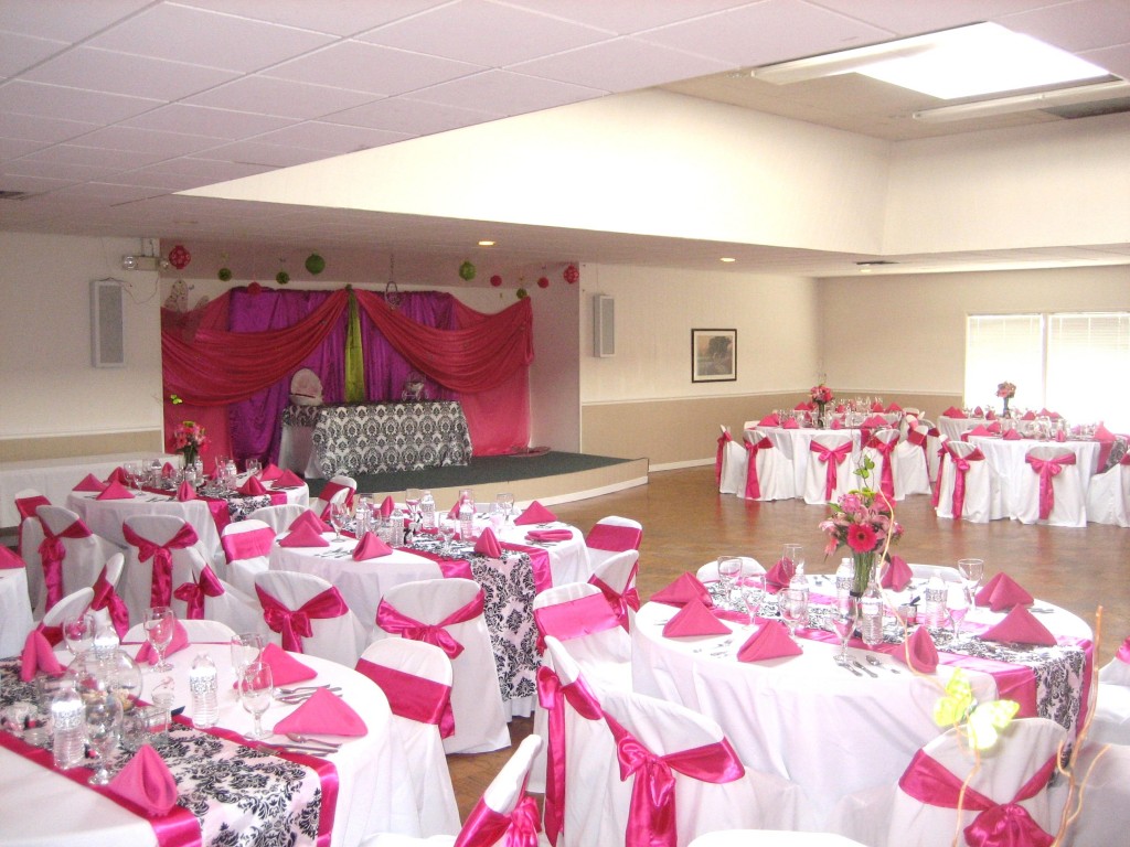Open and large community hall within the community center. Space for residents to host events and parties as pictured. Decorated for a residents events with multiple round tables surrounded by chairs decorated with a pink and white theme throughout.