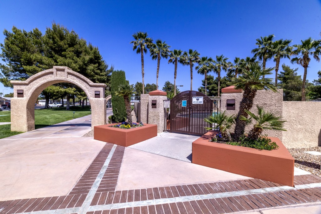 Gated entrance to pool area. Small palms planted at entrance. Large stone arch over paved walkway. Very tall palm trees in background.