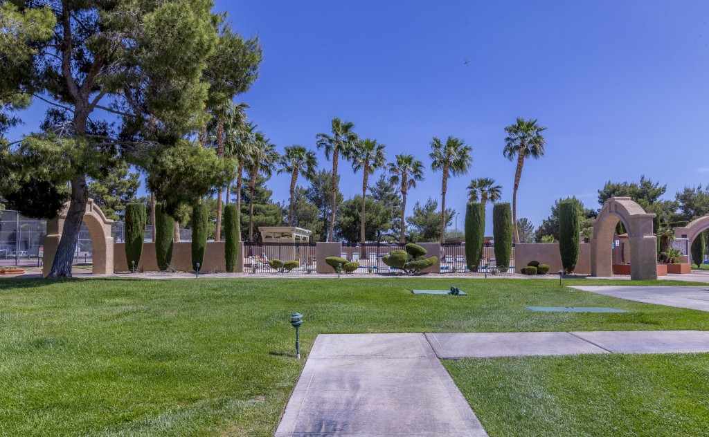 Lighted paved walkways amongst the trimmed green grass to the pool area. Large stone archways along the path. Tall trees and palm trees and trimmed shrubs.