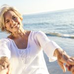 Happy senior man and woman couple walking or dancing and holding hands on a beach