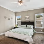 Bedroom with attached bathroom. Light gray walls with crown molding on top and bottom. Two windows. Queen sized bed with dark wood headboard and end table. Light brown carpeting.