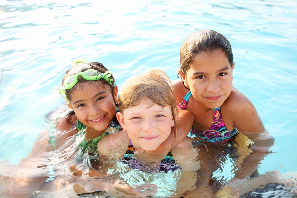 Three smiling girls swimming in pool.