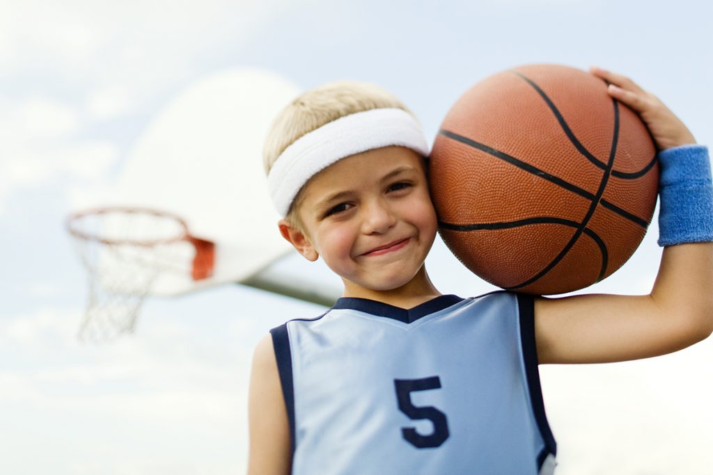 A young boy plays holds the basketball smiling.
