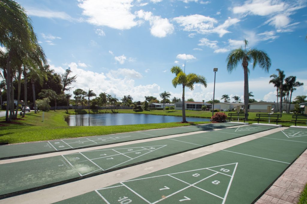 Palm Breezes Club has lots of amenities for its residents. Three shuffleboard courts are ready for play. Located next to lake. Bench seating at end of courts.