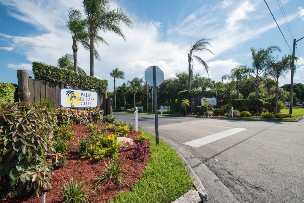 Palm Breezes Club has a well marked entrance with two signs on either side and flowing palm trees. Nicely landscaped with green grass and shrubbery.