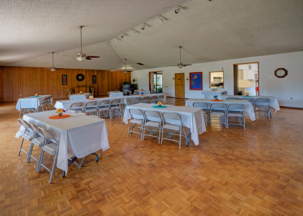 Ballroom set up with banquet tables and chairs. Vaulted ceiling with fans. White tablecloth.