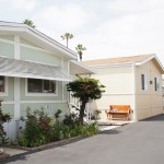 Manufactured home community with clean, paved streets and well maintained landscape. Light, neutral colored homes line the wide streets.
