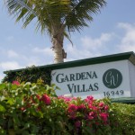 Gardena Villas, a manufactured home community located in Southern California. Greeted by an entrance filled with palm trees, pink and green flowers, and a concrete wall labeled Gardena Villas.