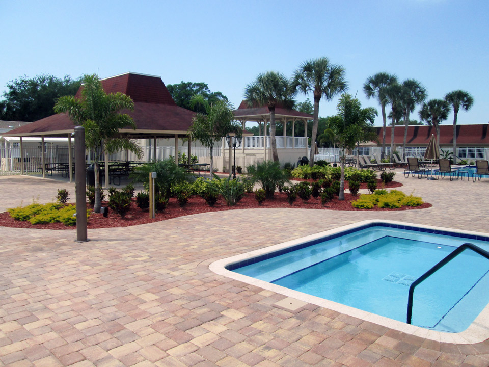 Large Jacuzzi. Two covered cabanas with picnic tables and chairs in the pool area and beautiful landscape with tall palm trees and small shrubs.