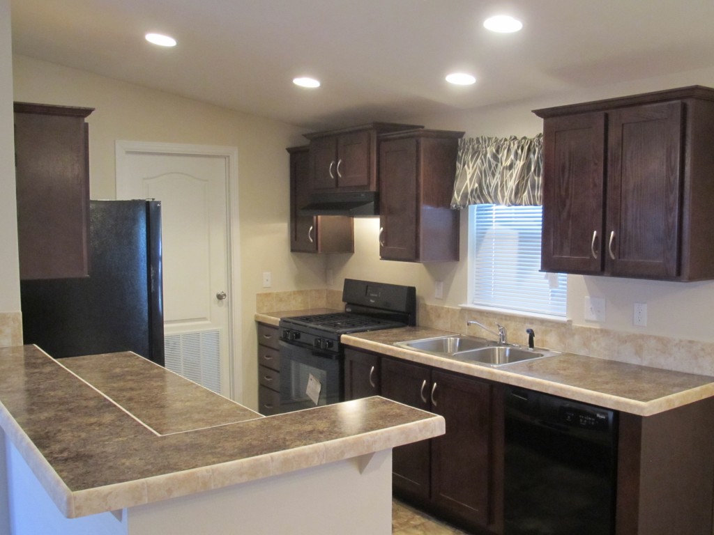 Interior view of a spacious kitchen with dark walnut cabinets, cream granite countertops, and black appliances.