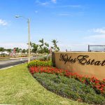 Front entrance to Naples with small, beige-yellow concrete wall with park name written on it. Beautiful landscape surrounds the sign with colorful flowers and clean-cut luscious grass.