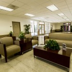 Community center connected to the leasing office with light cream walls and brown bordering. Comfortable seating area for residents to enjoy with a dark wood coffee table surrounded by two individual sofas with a side table and one love seat.