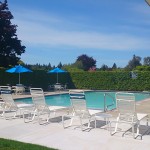 King Village, an all age manufactured home community, has swimming pool with lounge chairs, tables, and blue patio umbrellas.