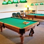 A billiards room with two pool tables with lighting above the tables.
