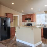 An open kitchen with all black appliances like a fridge, dishwasher and oven. wood cabinets and wood flooring with granite countertops and vaulted ceilings with recessed lighting.