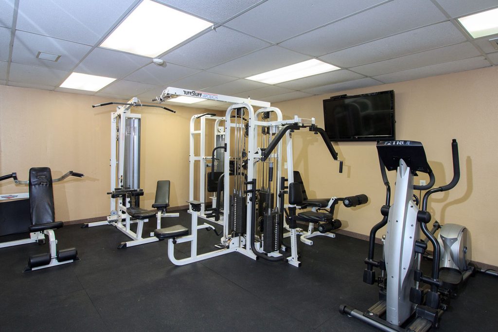 A fitness room with weight machines and flat screen TV on the wall.