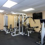 A fitness room with weight machines and flat screen TV on the wall.