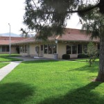 Southlake Mobiles community center, tree-lined and surrounded by luscious green grass. Well-maintained landscape and open walkways for easy access into the community center.