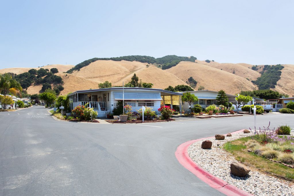 Clean and open street corner within the community. Green rolling hills encompass the background, with manufactured homes lining the streets.