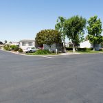 Wide corner street view within the senior community. Beautiful greenery line the streets with multiple manufactured homes.