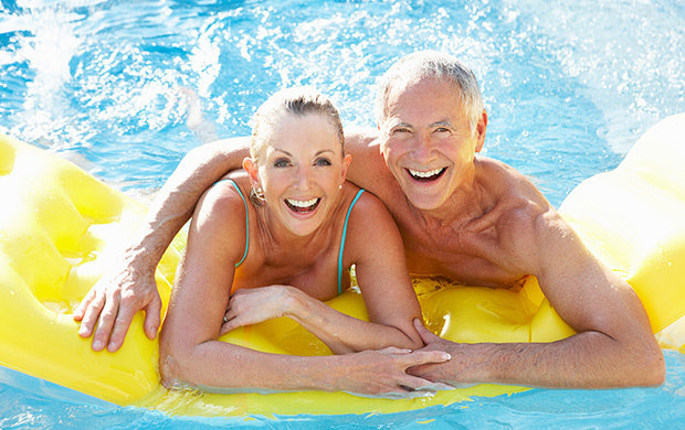 An active, mature man and woman enjoying the pool smiling away while on a yellow raft.
