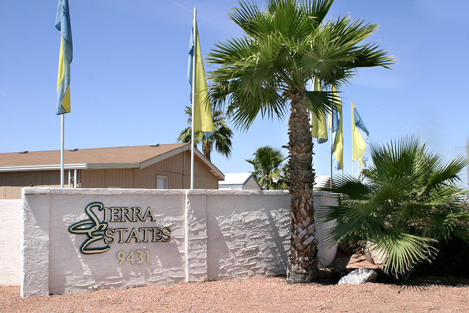 Sierra Estates entrance sign topped with blue and yellow flags
