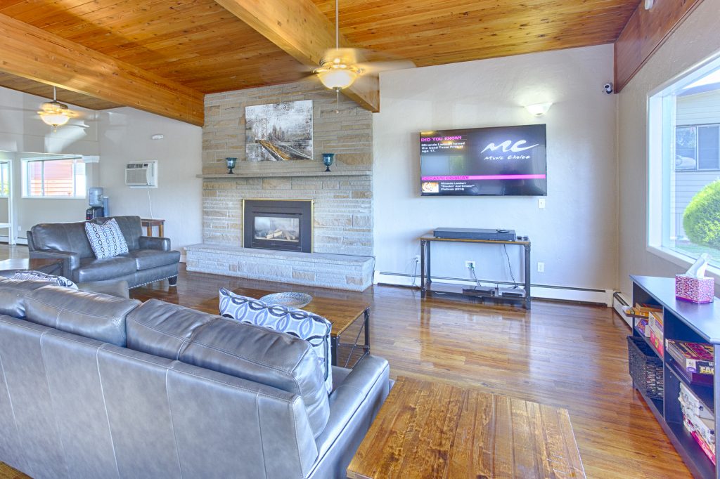 Modern and updated community center lounge. Beautiful, large stone fireplace and flat screen television make up the main wall. Light wood paneling on the high ceiling and matching wood, panel flooring create an open, cabin feel.
