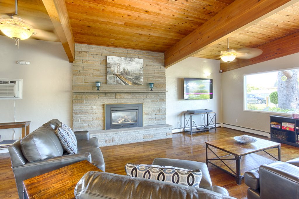 Beautiful, homey area in the community center with a flat screen television, beautiful, large, stone fireplace, and comfortable seating. High vaulted wood ceilings and matching wood flooring with a neutral, grey and black color scheme throughout.