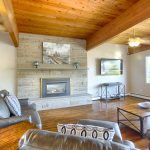 Beautiful, homey area in the community center with a flat screen television, beautiful, large, stone fireplace, and comfortable seating. High vaulted wood ceilings and matching wood flooring with a neutral, grey and black color scheme throughout.