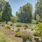 Peaceful waterfront view of Puyallup River, lined with beautiful tall trees and flowers. Benches and picnic tables also sit along the river.