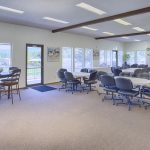 Open space community center enveloped by windows to enjoy natural light and the beauty of the outdoors. Equipped with circular tables surrounded by comfortable business chairs.