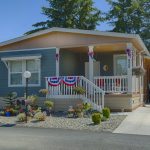 Beautiful manufactured home with small staircase leading up to covered porch. Painted with a shade of blue and decorated with an American flag theme. Side carport for one car coverage.