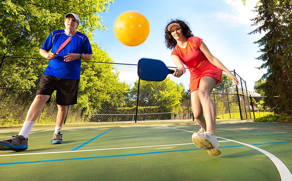 Retiree adult man and woman pickleball player in action. They are holding pickleball paddles posing to return the ball in a pickleball court.