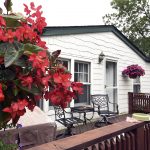 Rolling Hills Estates, an all age manufactured home community has homes with wood decks landscaped with colorful flowers of red and purple. Also a wrought iron patio set.