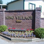 King Village sign on brick wall at entrance. Landscaped with small green shrubs and purple and red flowers.