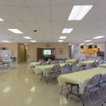 The Banquet Hall is set for an event with long tables, fold up chairs and yellow table cloths covering some tables.