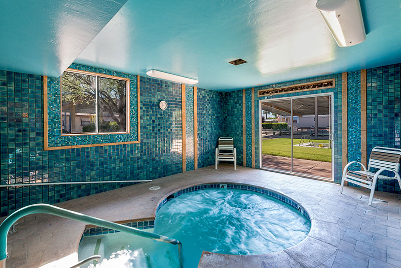 Beautiful indoor hot tub surrounded by blue tile walls and a light blue ceiling. Gold trimmings perimeter the windows and doors.
