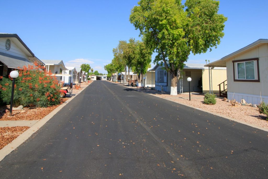 Large paved road surrounded by multiple, beautiful manufactured homes and greenery.