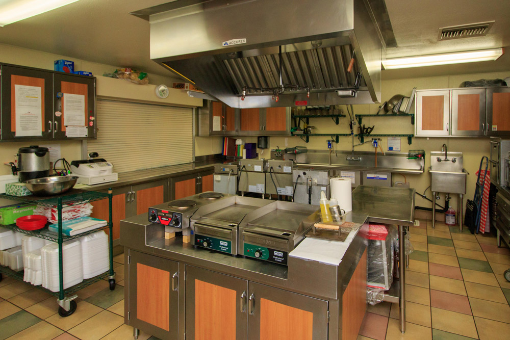 commercial kitchen with stainless steel griddles, sinks and smoke vents