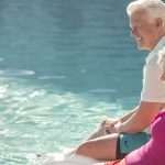 An older couple, man and woman, dipping there feet in the pool.